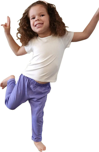 Smiling child in sensory-friendly purple pants and white t-shirt jumping playfully