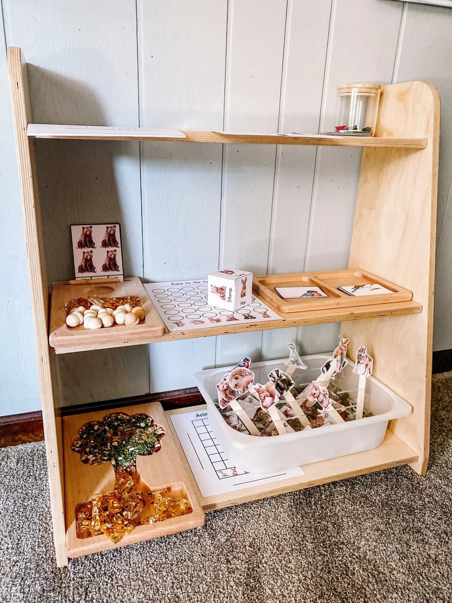 Tiered wooden toy shelf with sensory learning materials and animal activity bins in a playroom.