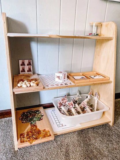 Tiered wooden toy shelf with sensory learning materials and animal activity bins in a playroom.