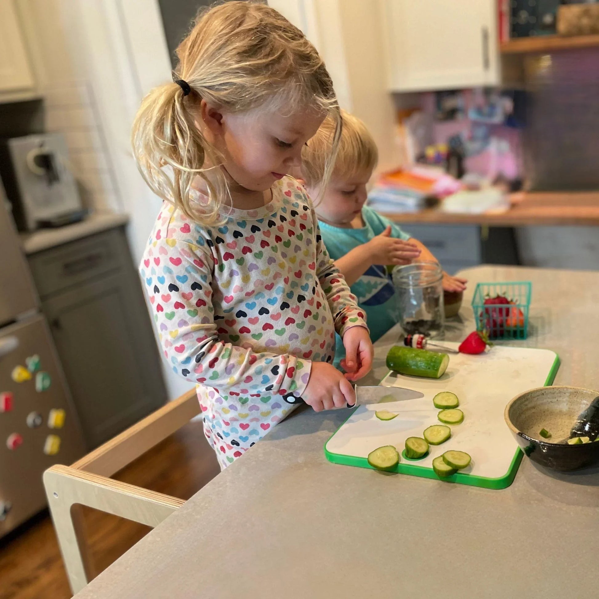 Young children slicing cucumber on kitchen counter, learning and practicing life skills