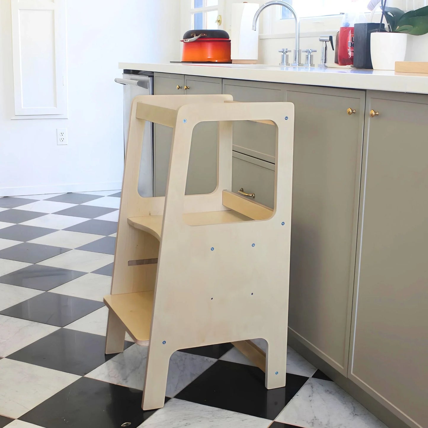 Wooden learning tower for kids beside kitchen counter on checkered floor