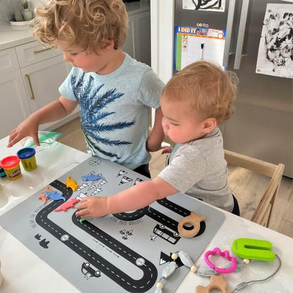 Two children playing with sensory toys and Play-Doh on a themed activity mat in a kitchen