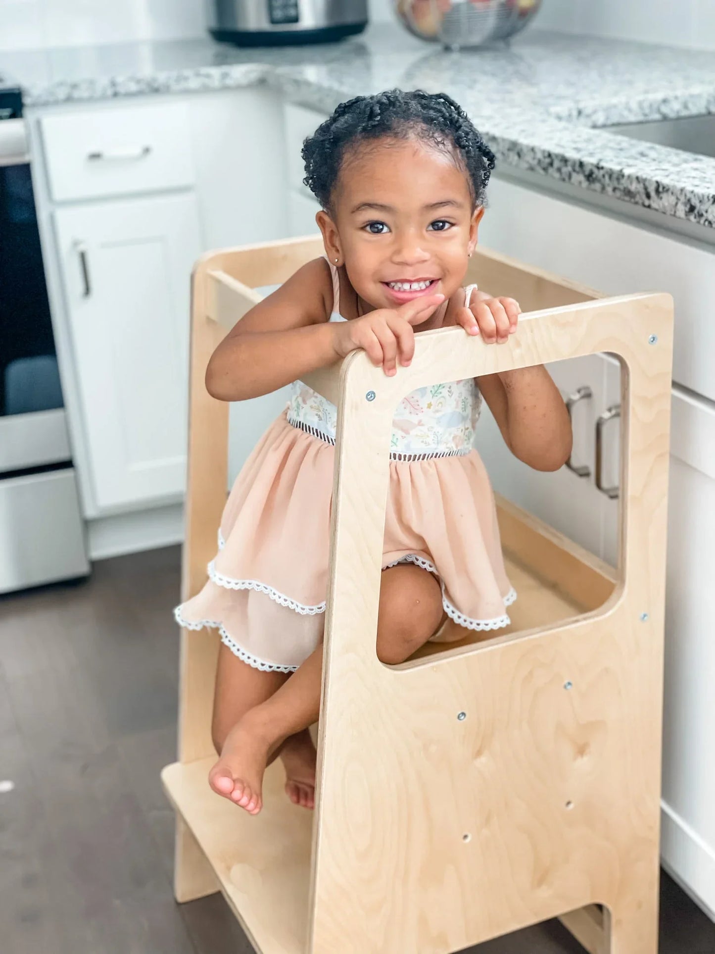 Smiling toddler sitting in a wooden learning tower in a modern kitchen