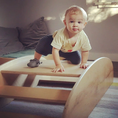 Toddler climbing on wooden sensory rocker toy in a cozy playroom