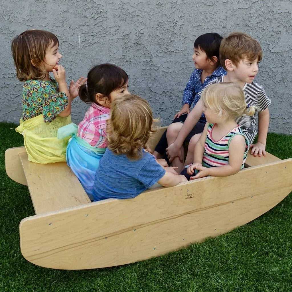 Children playing together on a wooden sensory rocking boat outdoors on grass.
