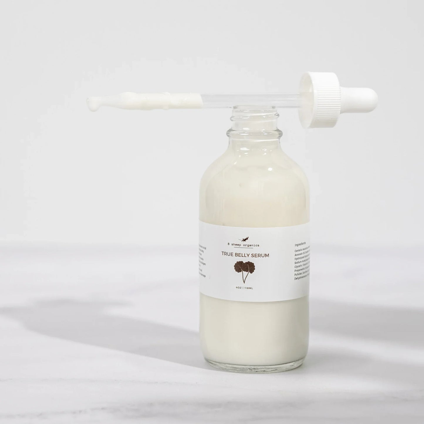 Glass bottle of True Belly Serum with dropper, creamy texture, minimalist background