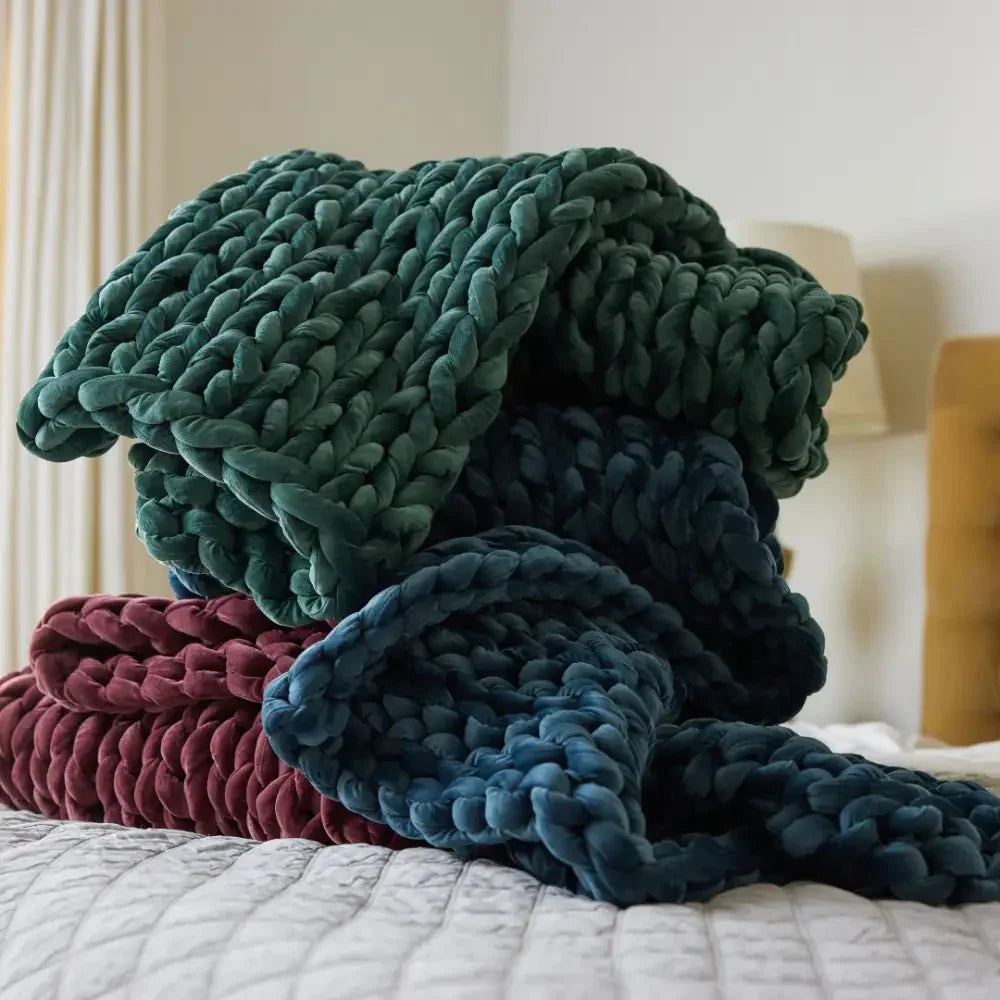 Chunky knit weighted blankets in green, blue, and burgundy stacked on a bed