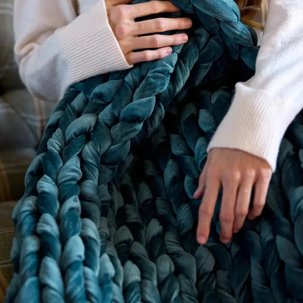 Hands holding chunky sapphire blue velvet weighted blanket on a sofa