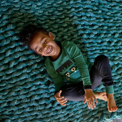 Smiling child lying on chunky emerald green velvet weighted blanket