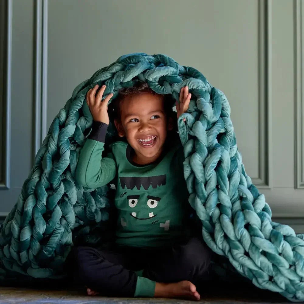 Smiling child under chunky emerald velvet weighted blanket, sensory-friendly and cozy