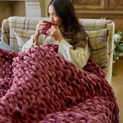 Woman relaxing on couch with chunky ruby velvet weighted blanket, holding mug