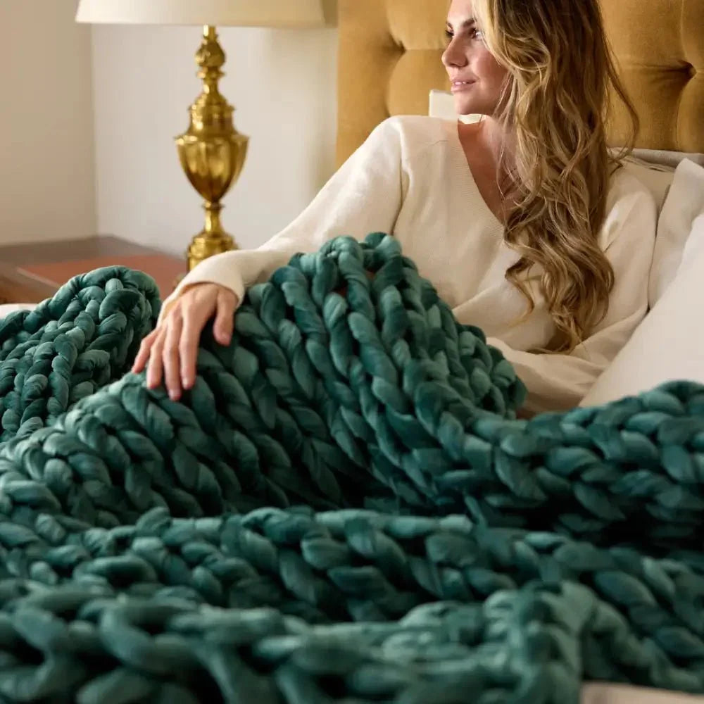 Woman relaxing with a chunky emerald velvet weighted blanket on bed, cozy bedroom setting