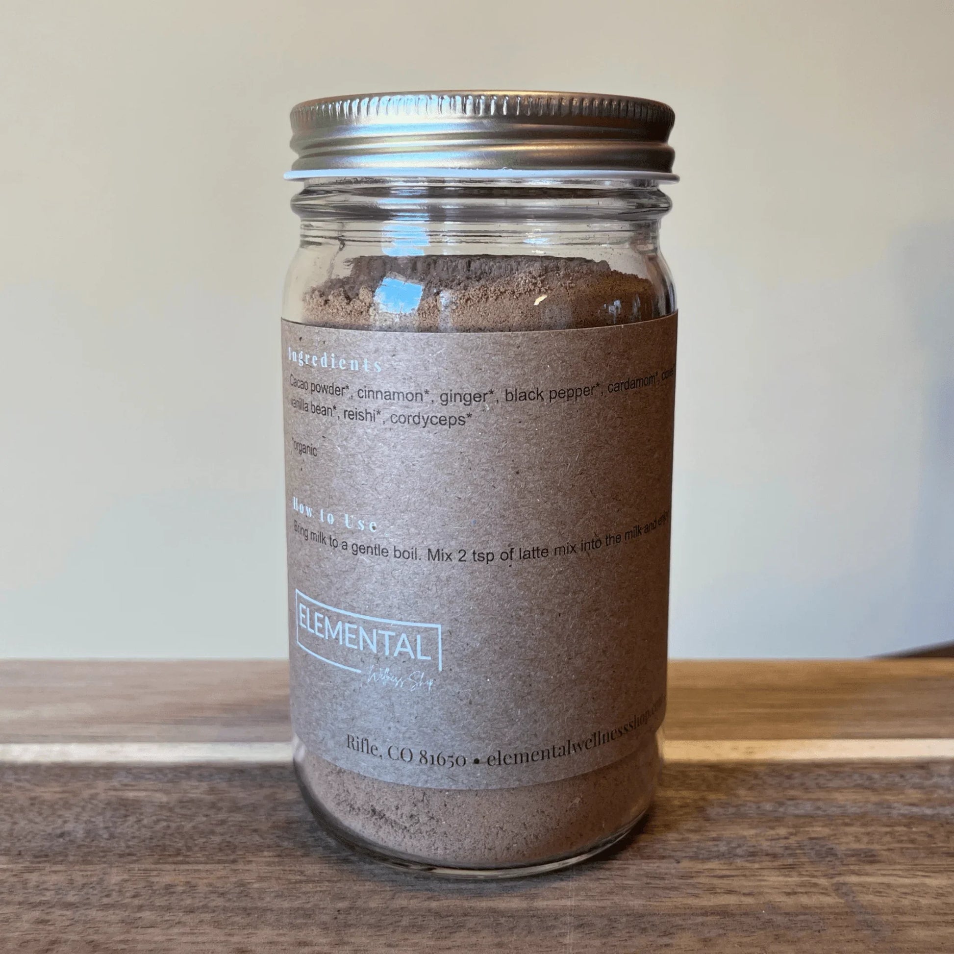 Glass jar of cacao chai latte mix with brown label on wooden surface