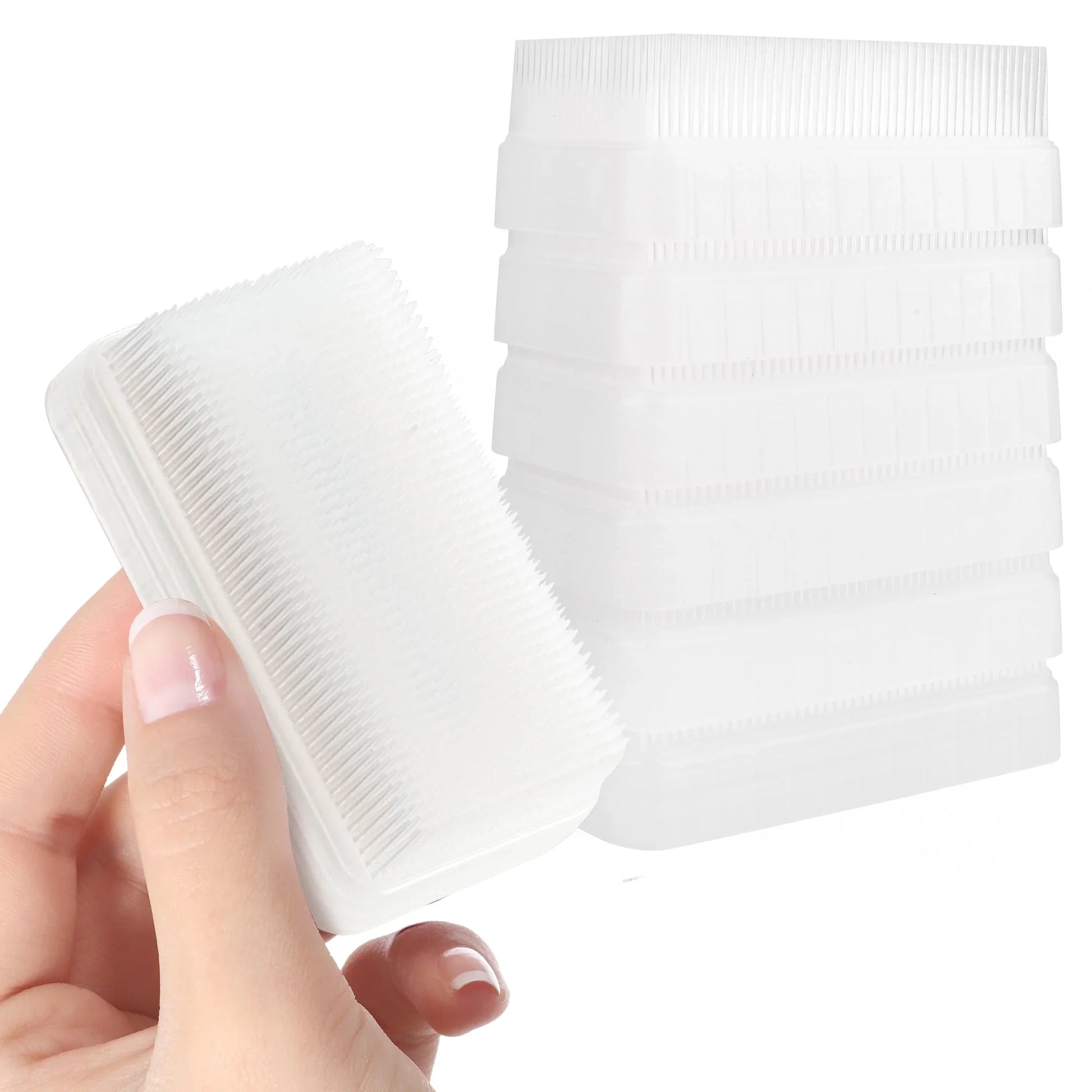 Hand holding a white sensory brush with soft bristles, stack of sensory brushes in background