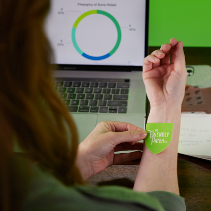 Person wearing a green patch on their wrist with a laptop displaying a graph in the background